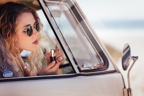 Una ragazza mette il rossetto allo specchio della macchina foto iStock.